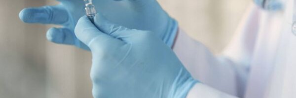 Person mit medizinischen Handschuhen hält Ampulle 