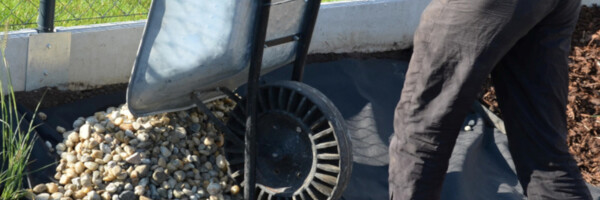 Mann schüttet Steine mit Schubkarre auf ausgelegtes TERRAM Rootguard Trennvlies