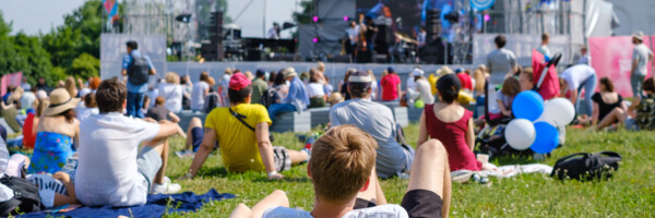 Sitzende und liegende Festivalbesucher auf dem Grün vor einer Bühne
