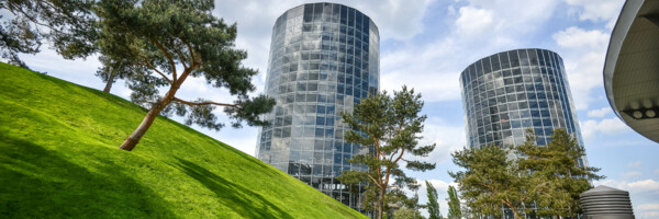 Weg führt an grünem Hang entlang zu 2 Glasgebäuden