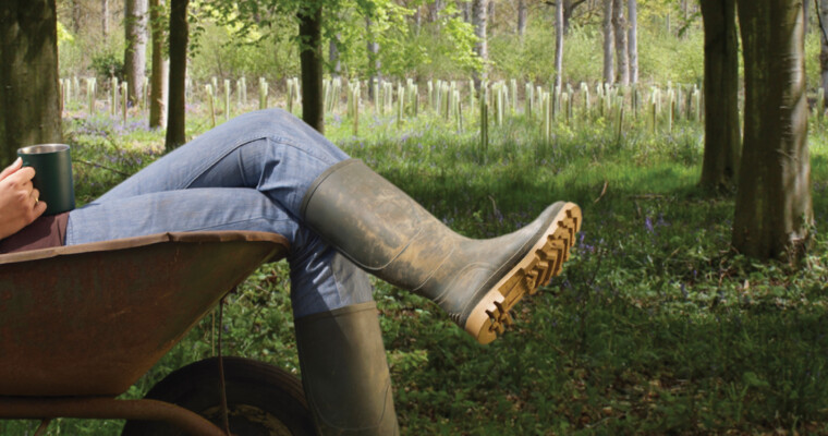 Ein sitzender Mann mit Gummistiefeln und im Hintergrund eine Reihe von Wuchshüllen.