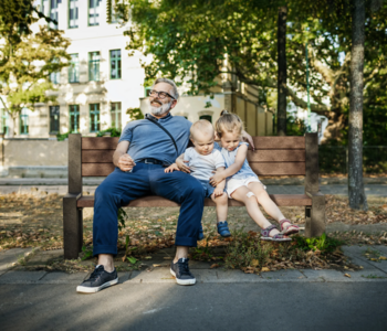 Familie sitzt auf brauner Hyde Park Bank aus hanit Recyclingkunststoff in einer grünen Stadt.