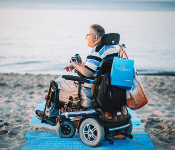 Elektrischer Rollstuhl fährt zum Wasser auf blauer TerraMat Sandmatte