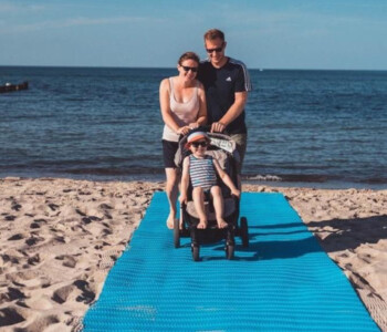 Familie schiebt Kinderwagen über den barrierefreien Strandweg